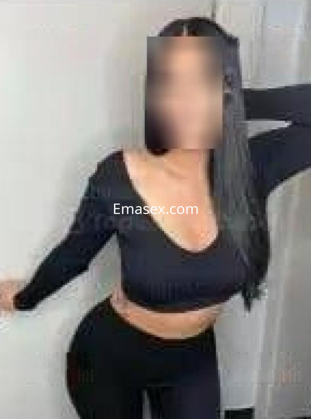 Puta con cabello largo y lacio, viste un conjunto negro que resalta su figura en un ambiente minimalista de Madrid.