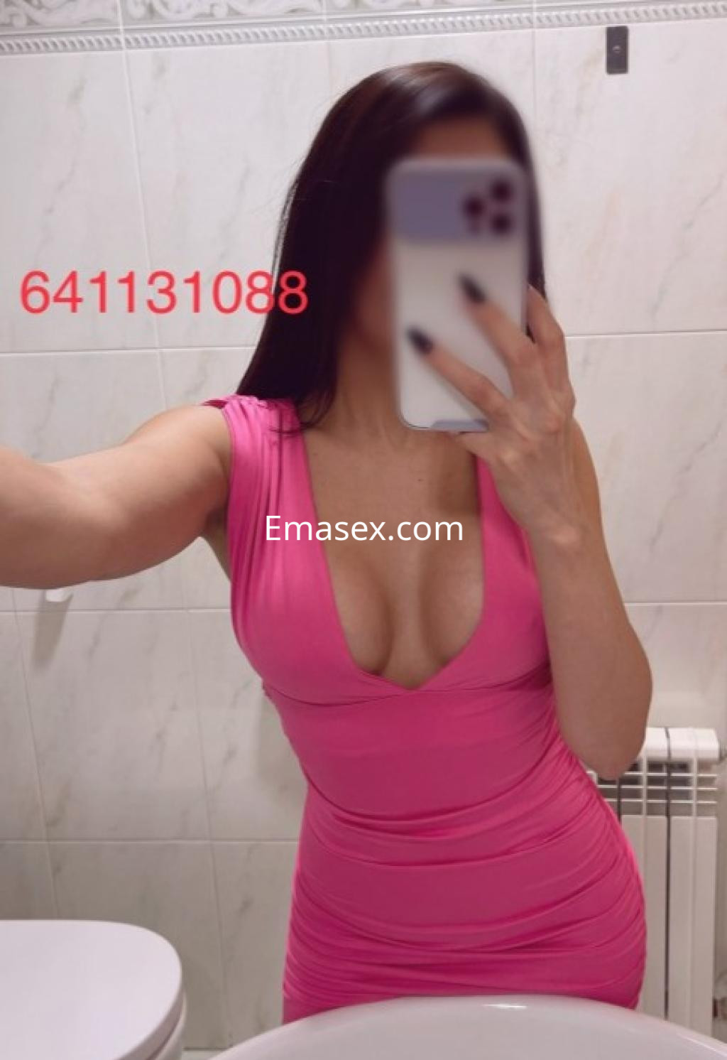 Escort en Lleida, con un vestido rosa ajustado y un escote pronunciado, posando frente a un espejo.