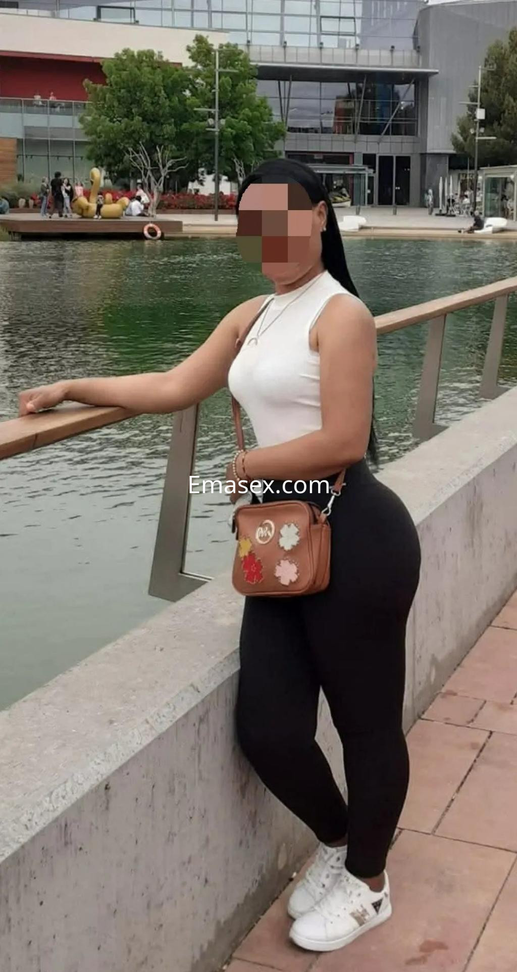 Puta de pie junto a un canal en Zaragoza, vistiendo camiseta blanca y leggins negros, con bolso y zapatillas.