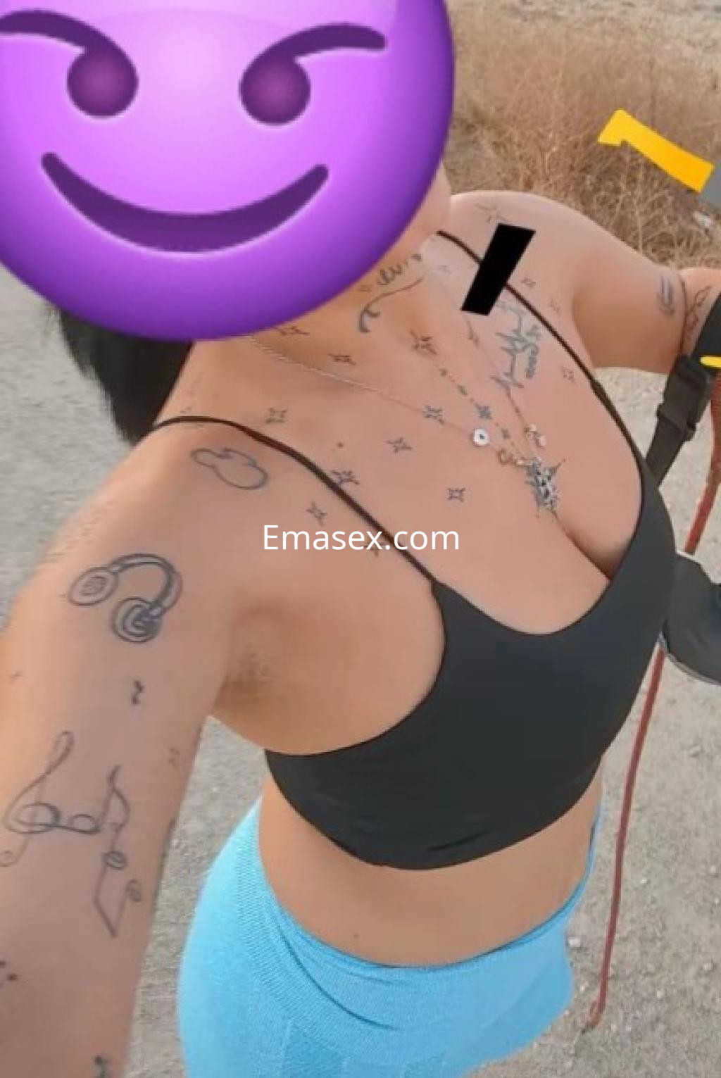 Puta en Huelva lleva un top negro y leggings azules, mostrando tatuajes en su piel mientras sonríe.
