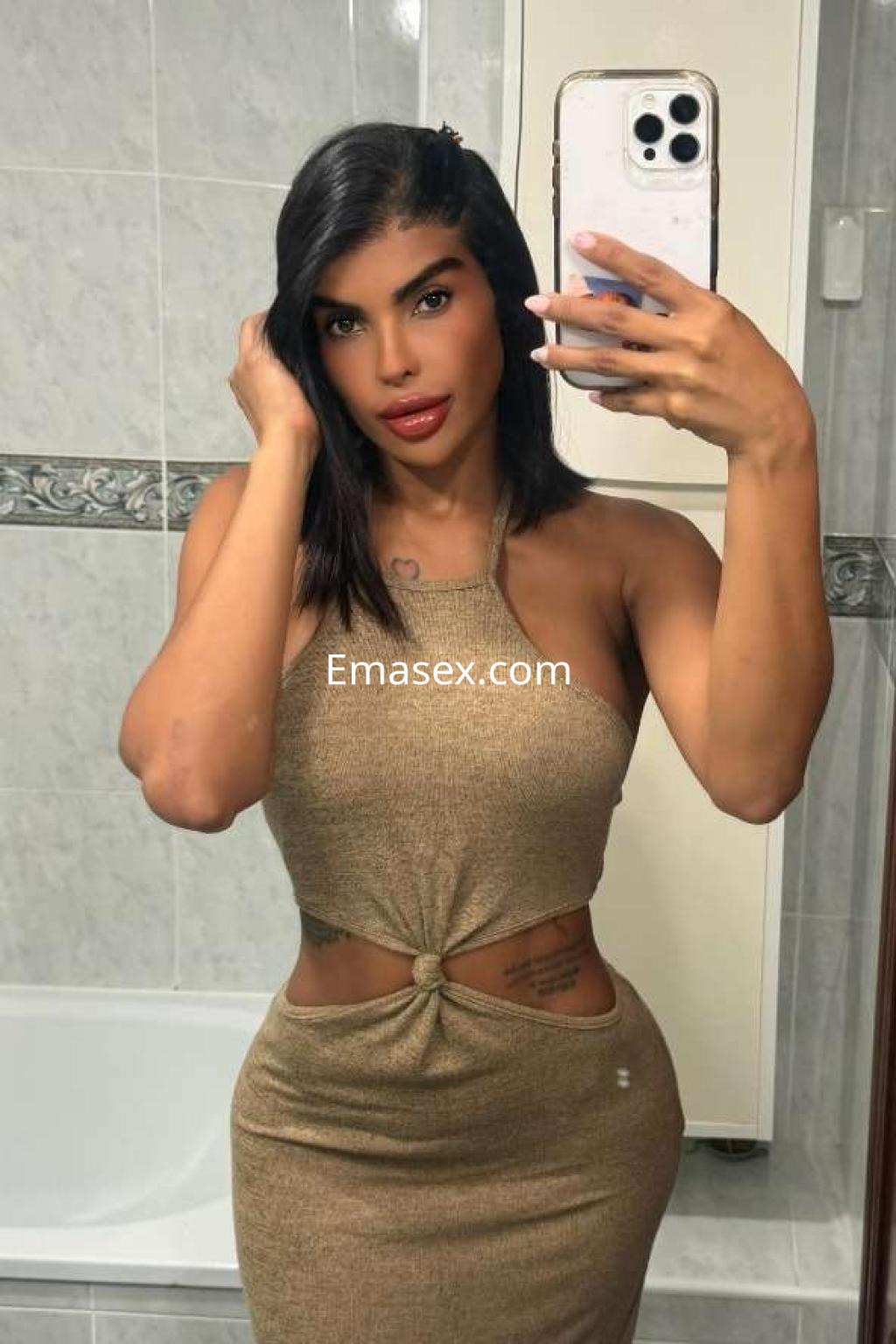 Escort en Ibiza con cabello oscuro y lacio, vistiendo un vestido ajustado color dorado y posando frente a un espejo.