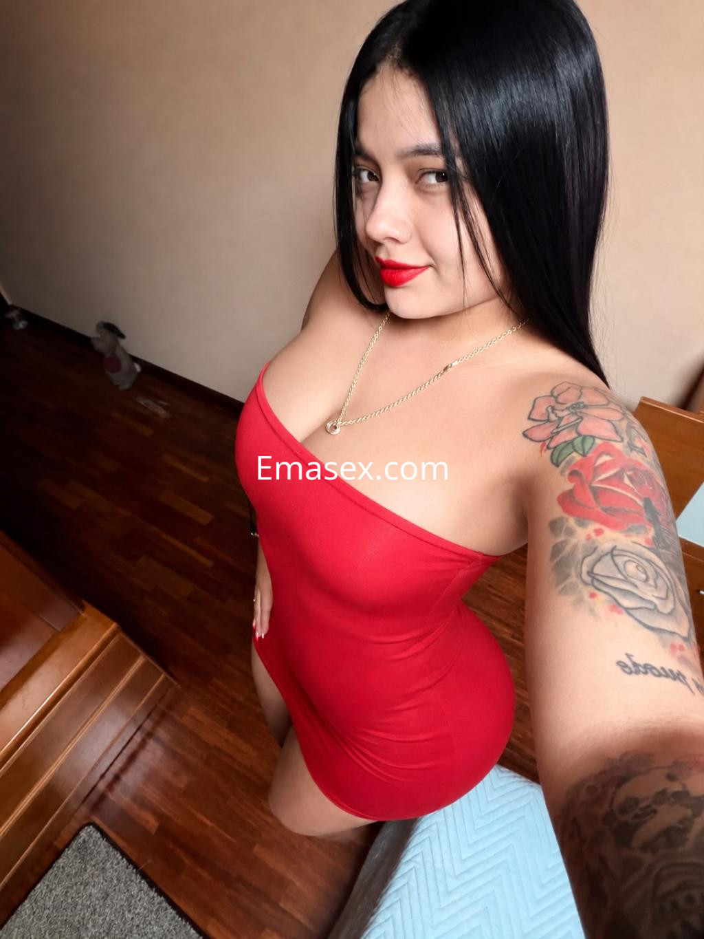 Escort en Vitoria con vestido rojo ajustado, cabello largo y liso, mostrando un tatuaje en el brazo y posando con actitud.