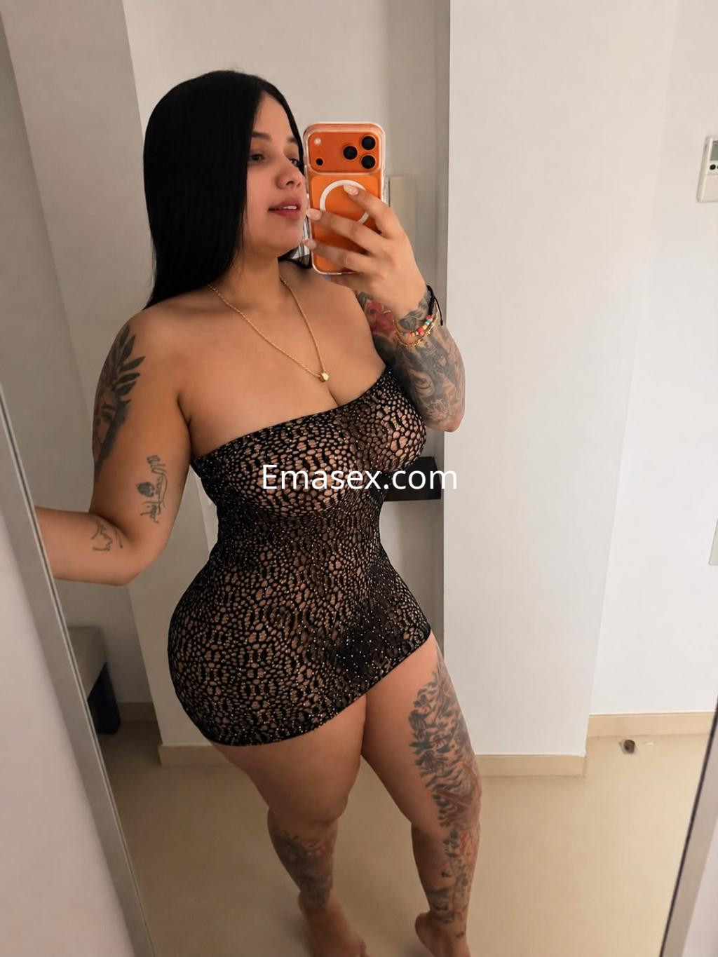 Escort en Vitoria con vestido negro de encaje ajustado, cabello largo y liso, posando frente a un espejo.