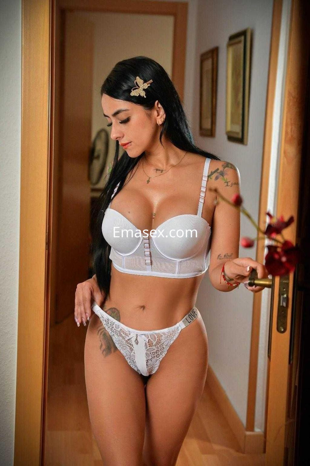 Escort en Alicante luciendo lencería blanca y posando de perfil en un ambiente acogedor.