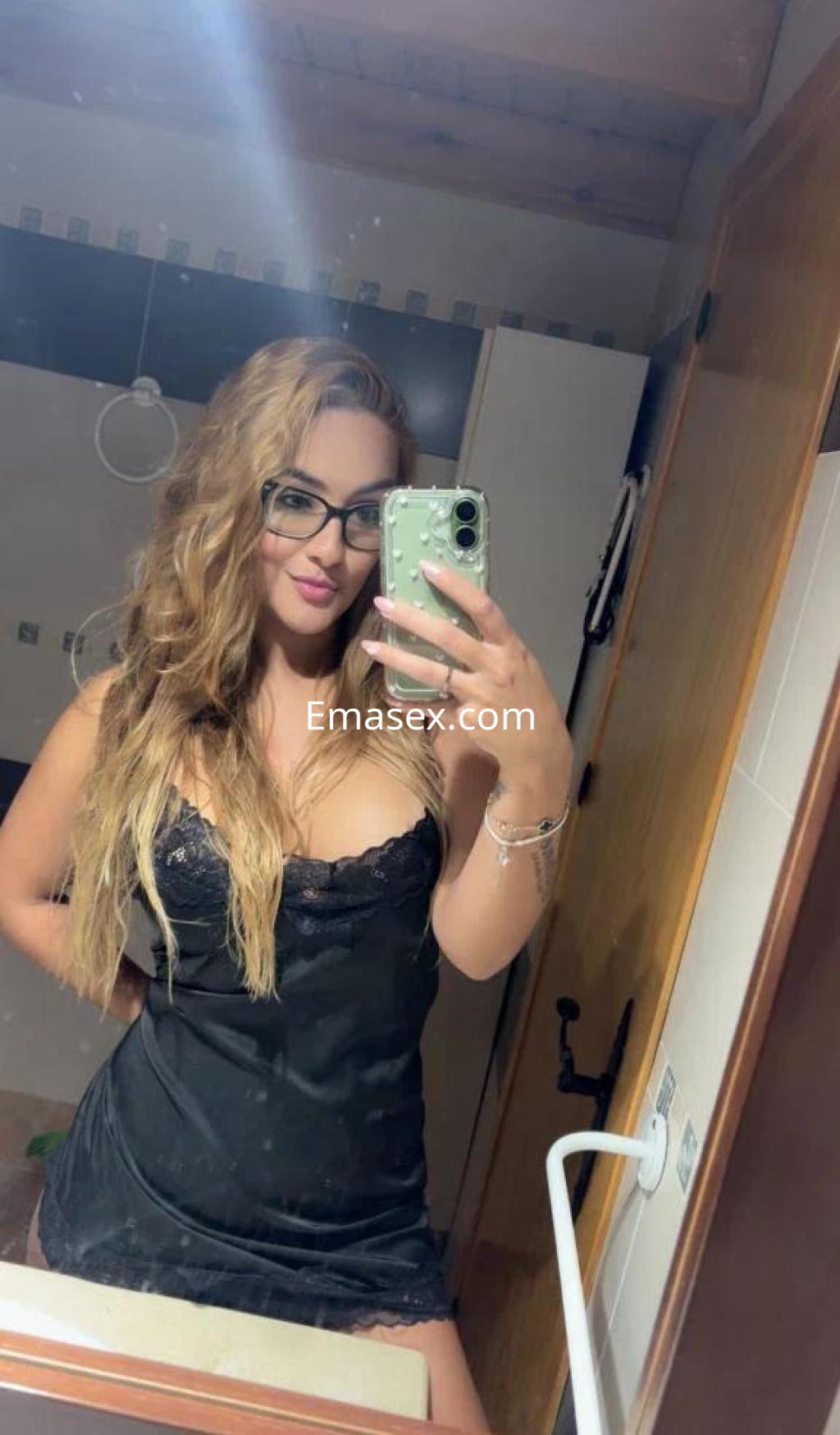 La puta aparece en un baño con cabello largo y ondulado, vistiendo un vestido negro y gafas.