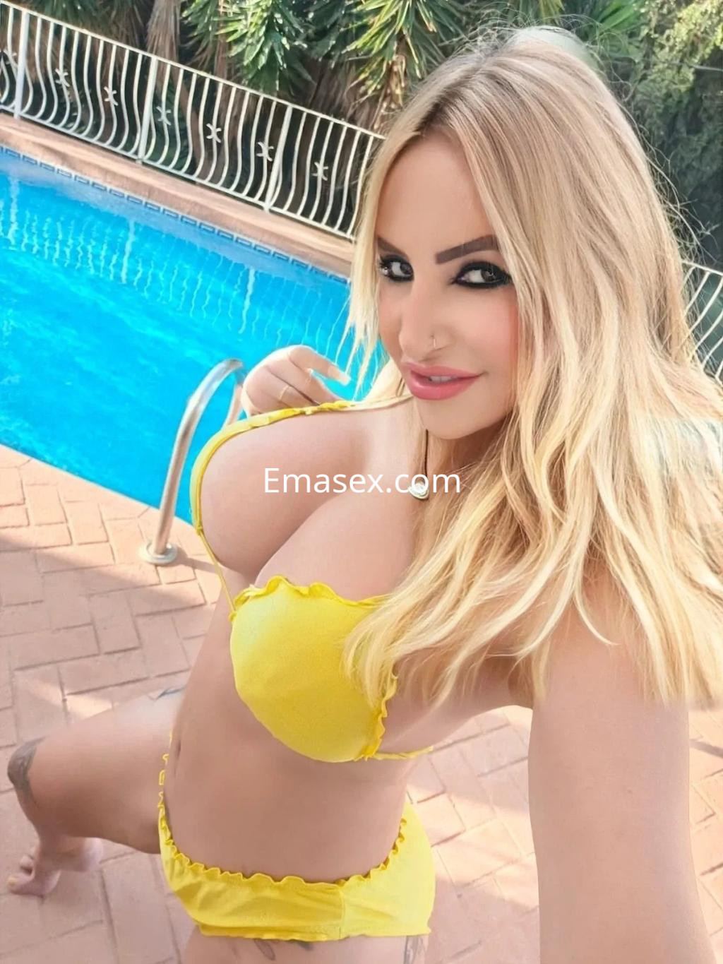 Escort en Alicante posando con un bikini amarillo junto a una piscina, mostrando su cabello rubio y una sonrisa.