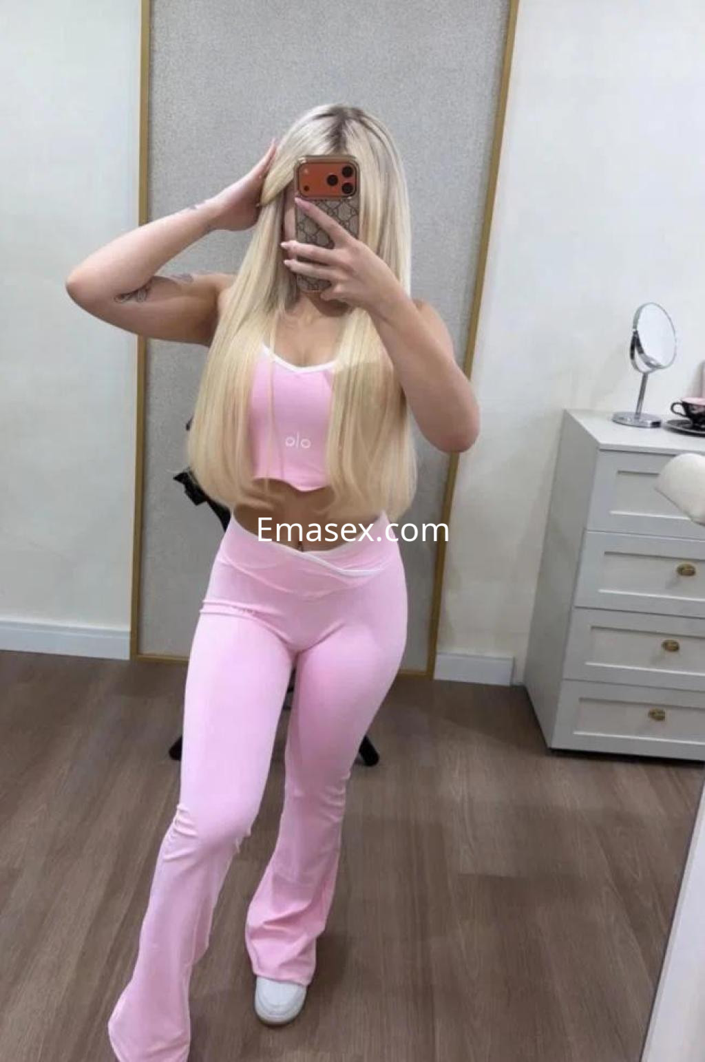 Puta en Córdoba luce un conjunto deportivo rosa, mostrando su largo cabello rubio y posando en un interior moderno.