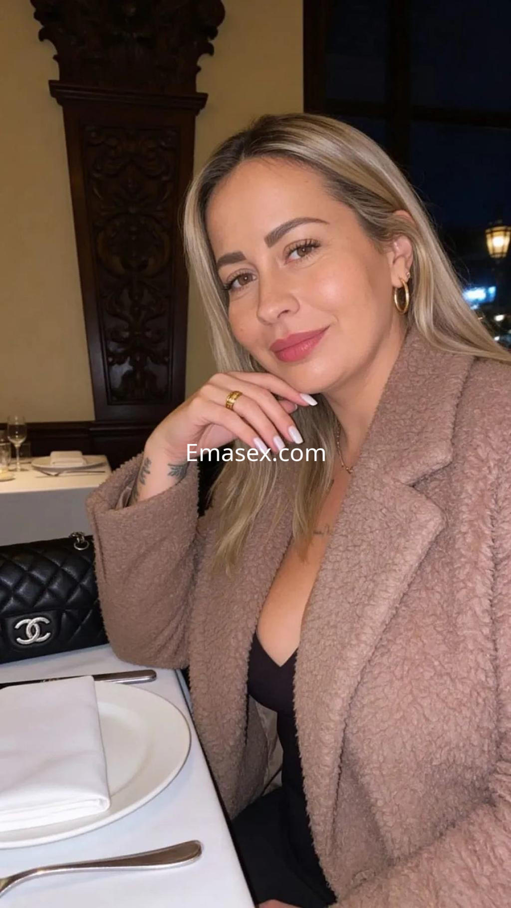 Escort con cabello rubio y lacio, vestida con un abrigo beige, sonríe en un ambiente elegante en Córdoba.