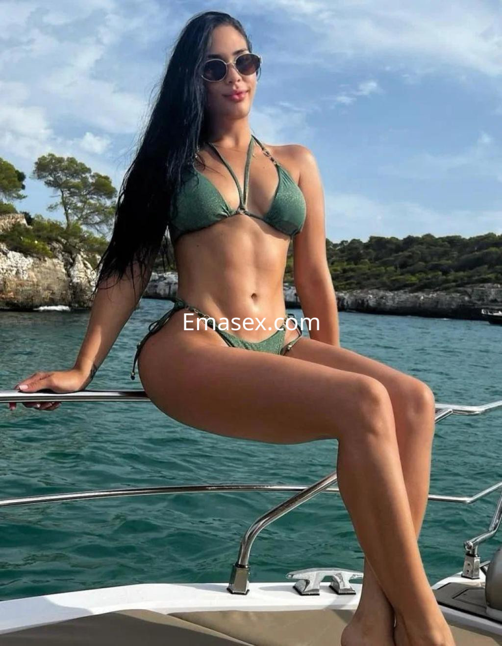 Escort en Marbella luciendo un bikini verde, sentada en la proa de un barco frente al mar.