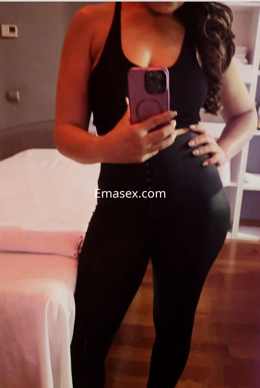 Puta en Oviedo posando con un top negro y pantalones ajustados, mostrando su figura en un ambiente interior.