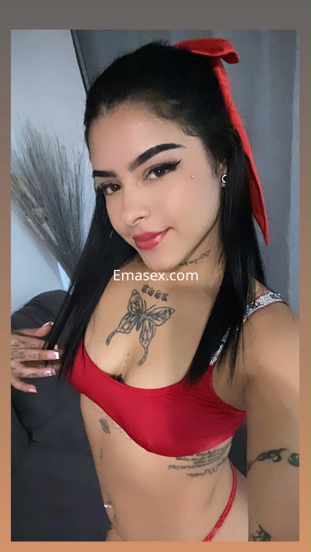 Escort en Madrid con cabello negro, luciendo un top rojo y un lazo en la cabeza, posando con una sonrisa.