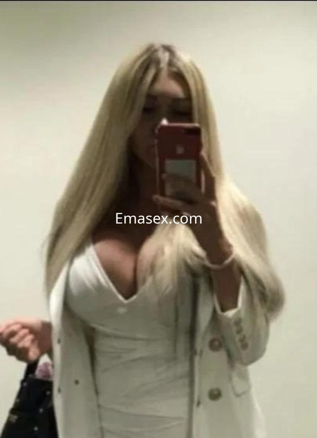 Escort en Almería con cabello largo y rubio, vistiendo un vestido blanco y sosteniendo un bolso negro.