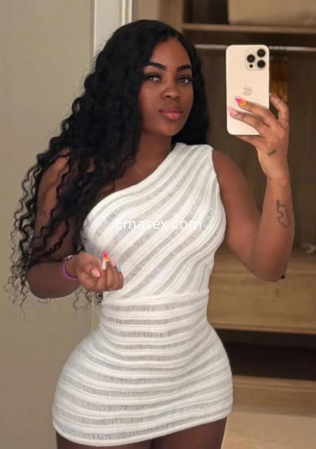 Puta posando con un vestido blanco de un solo hombro, en un entorno interior con cabello rizado en Almería.