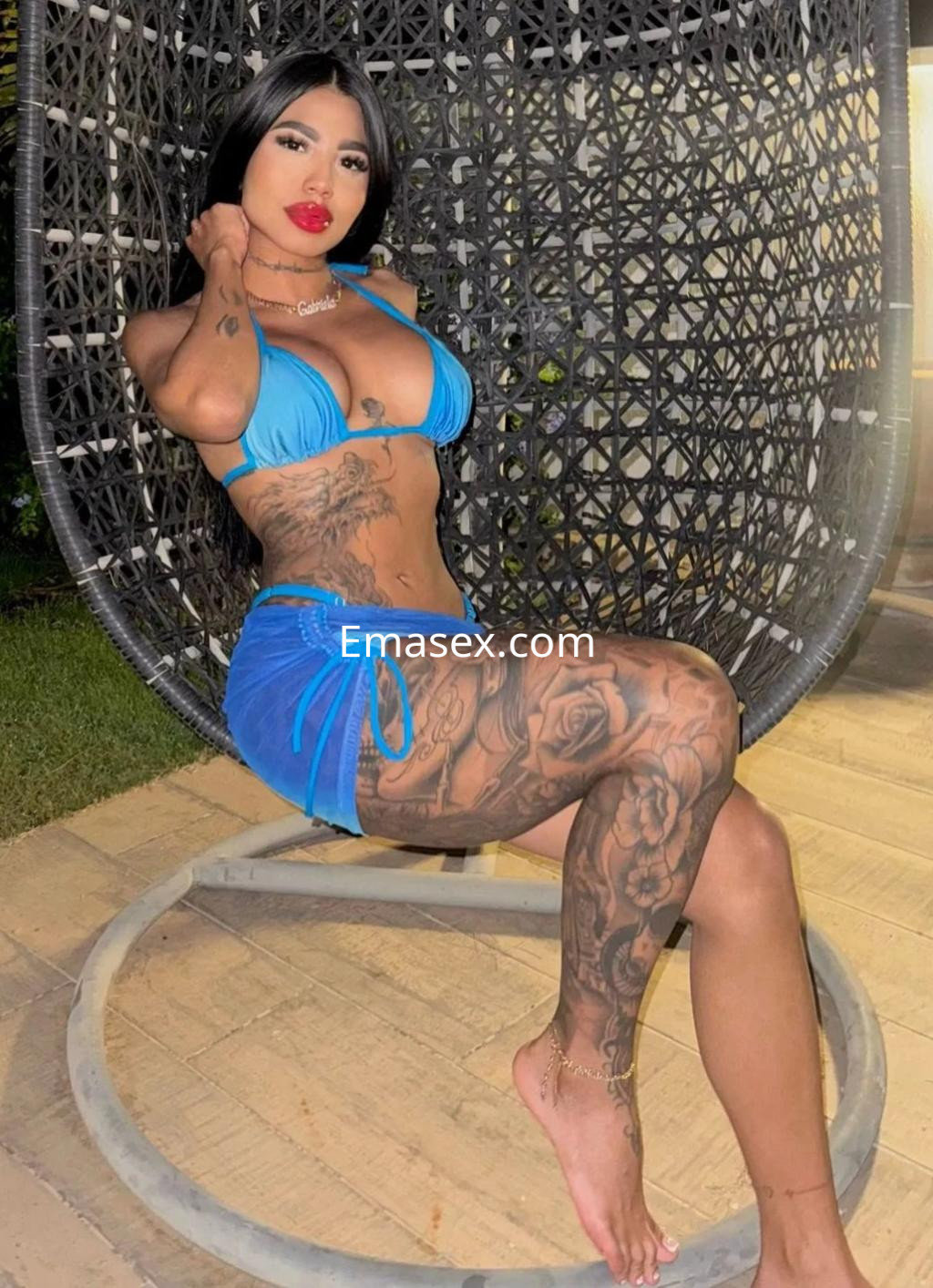 La puta de Málaga posa con un bikini azul y una falda corta, mostrando sus tatuajes en un entorno acogedor.