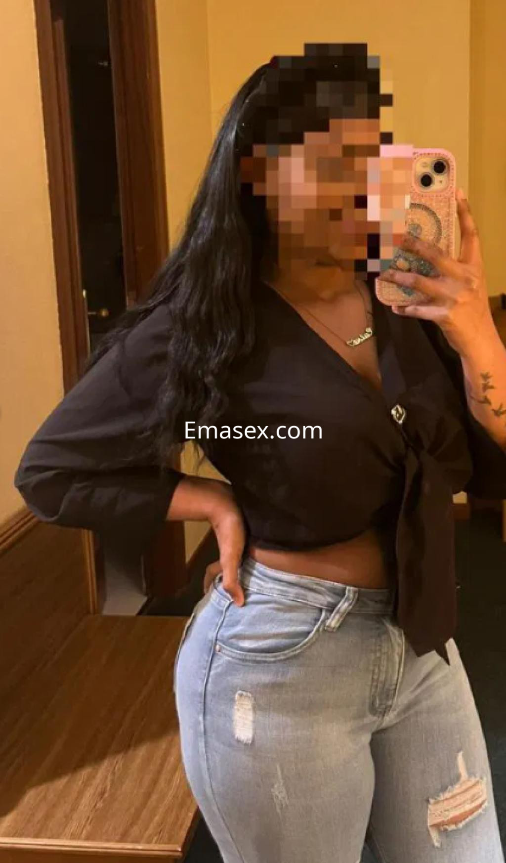 Escort en Pamplona posando frente a un espejo, con blusa negra y jeans ajustados, mostrando una sonrisa.