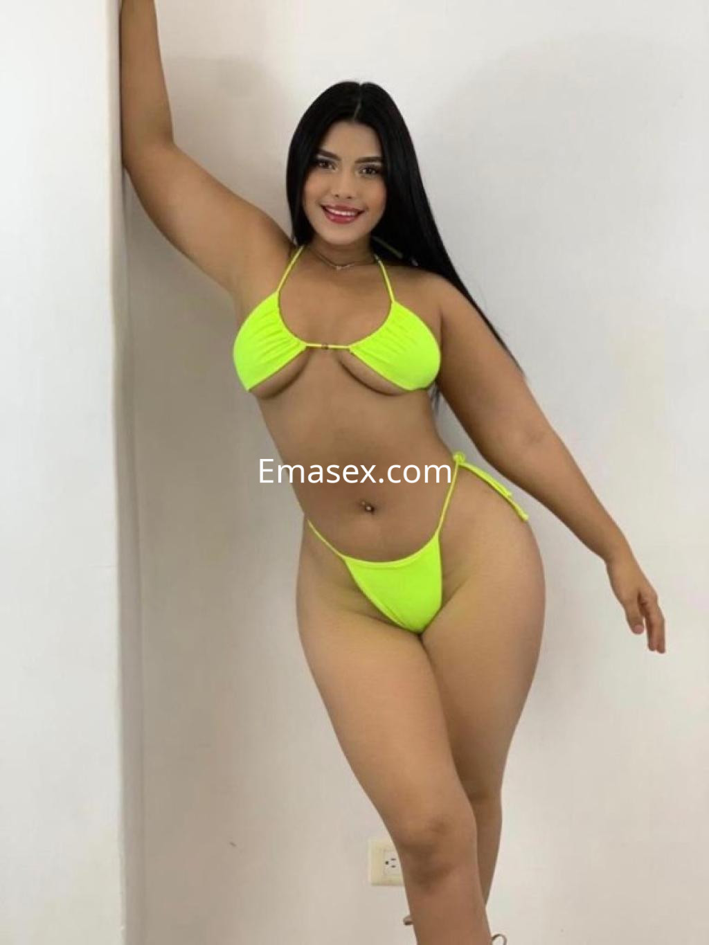 Puta de cabello largo y lacio en bikini amarillo fosforescente, posando con una mano en la pared en Sevilla.