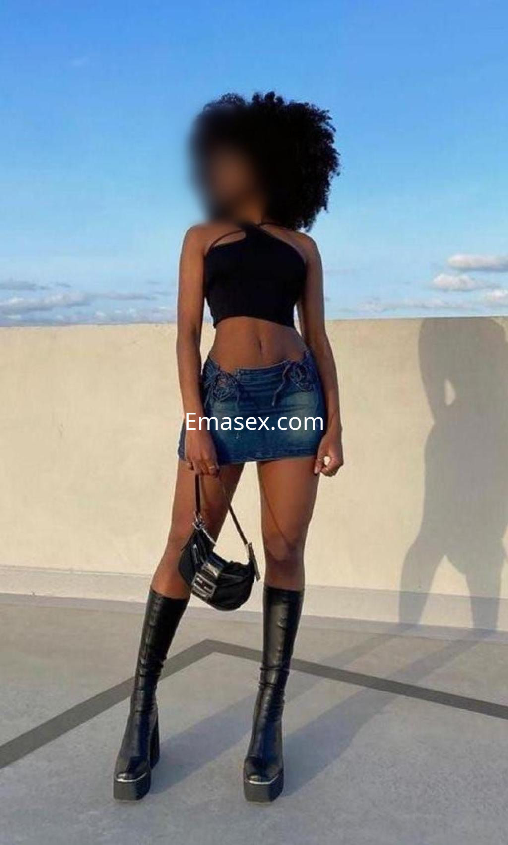 Escort en Pamplona con top negro y mini falda de mezclilla, luciendo botas altas y peinado rizado.