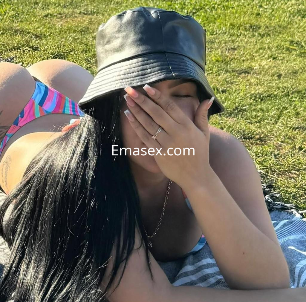Puta recostada sobre el césped en Santiago, con un sombrero negro y una bikini de colores, cubriendo su rostro.