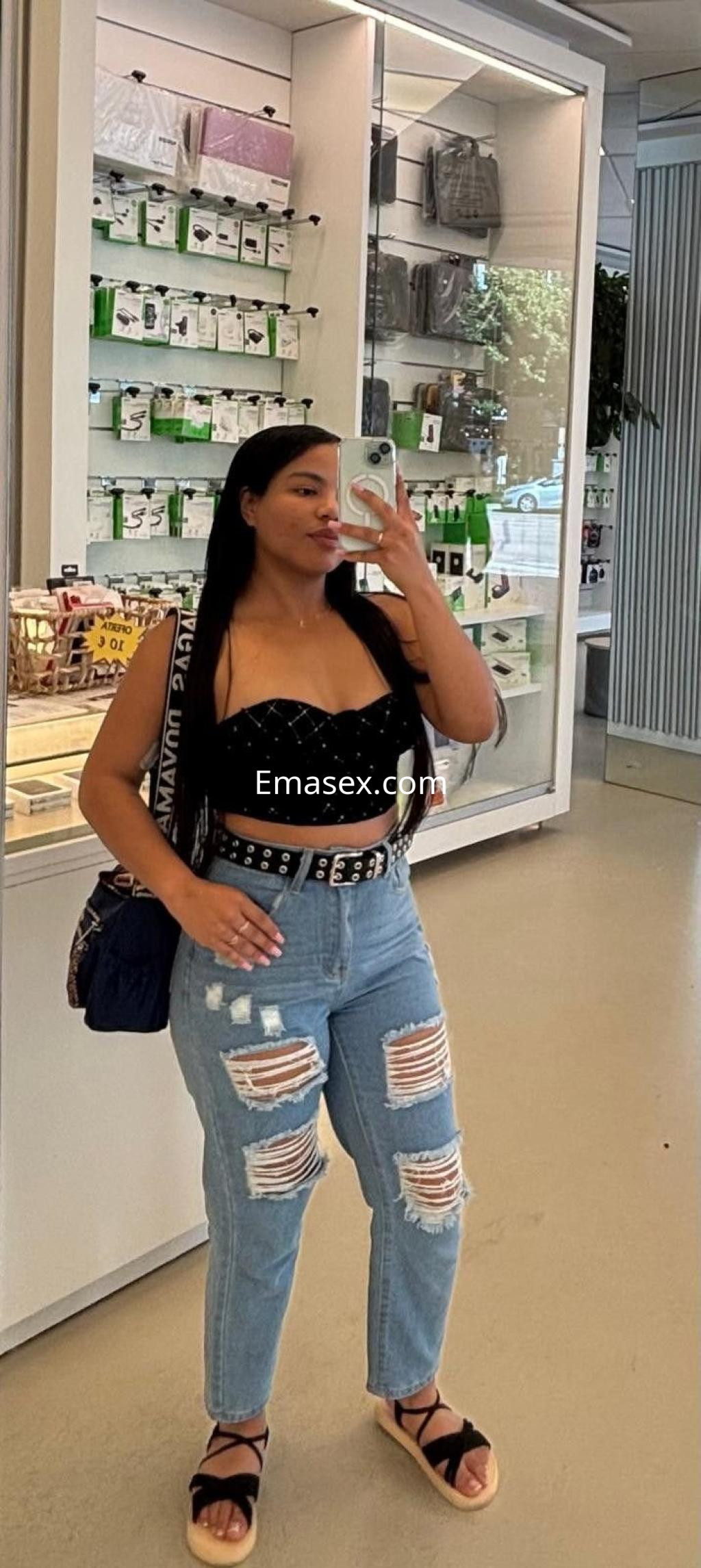 Puta en Burgos, con blusa negra y jeans rasgados, posando frente a un espejo en una tienda.
