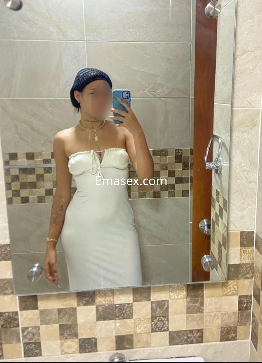 Escort en Cáceres posando en un baño con un vestido blanco ajustado y un peinado recogido.