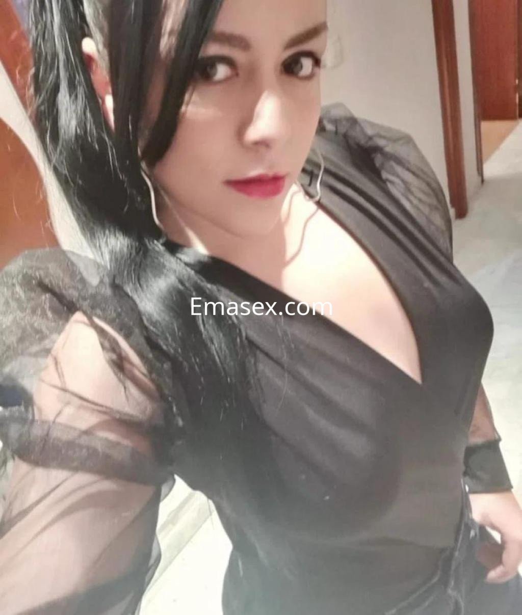 Escort en Cáceres con cabello largo y oscuro, luciendo una blusa negra transparente y un look elegante.