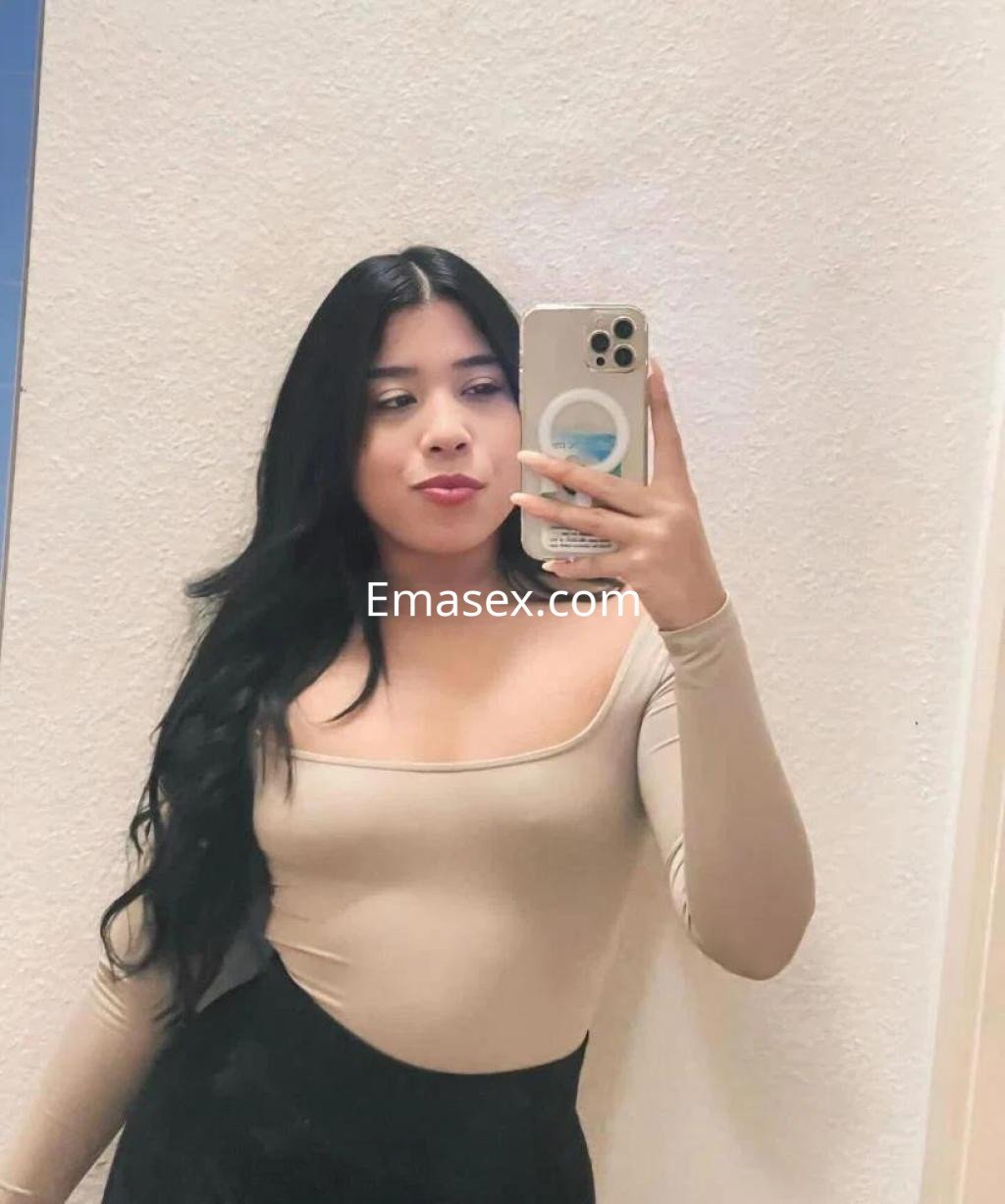 Escort en Coruña, con cabello largo y negro, viste un body claro y falda negra mientras se toma una selfie frente a un espejo.