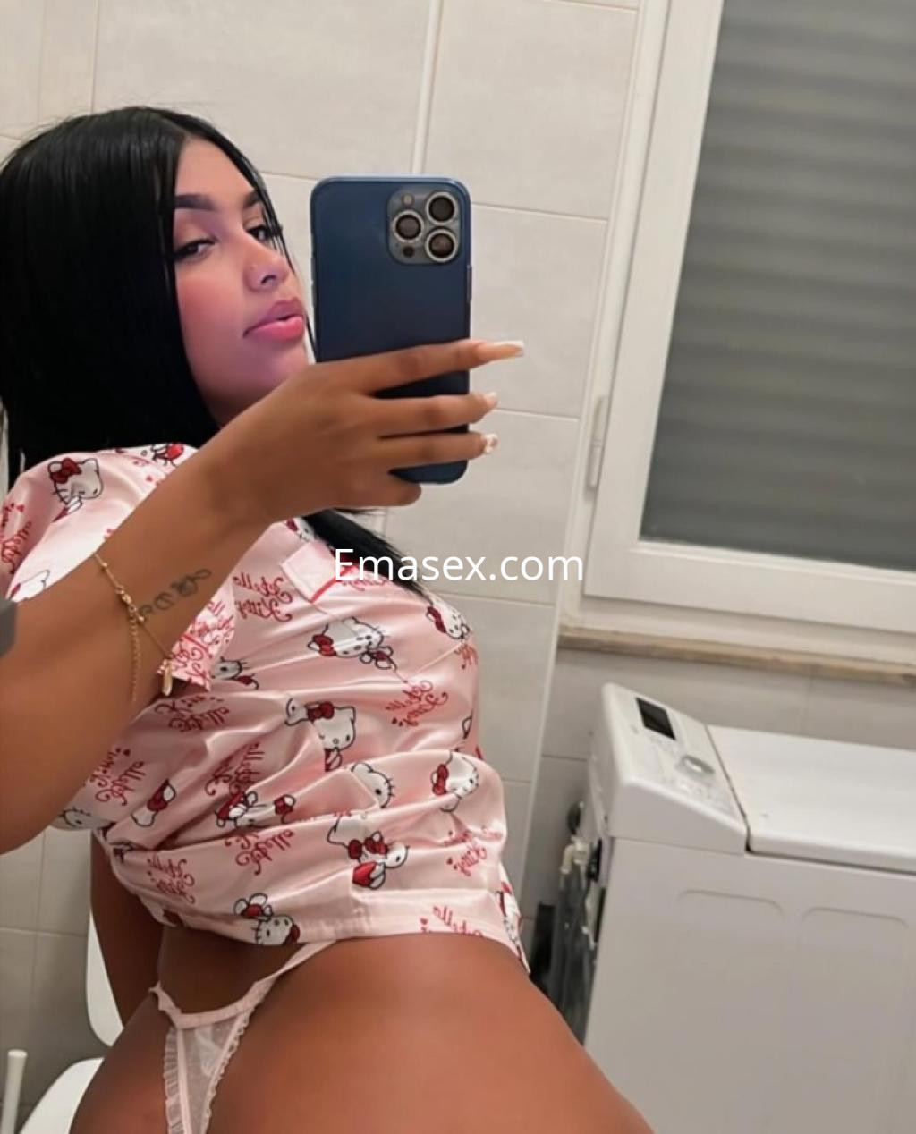 Puta en León se toma un selfie en el espejo luciendo una blusa rosa con estampado y lencería blanca.