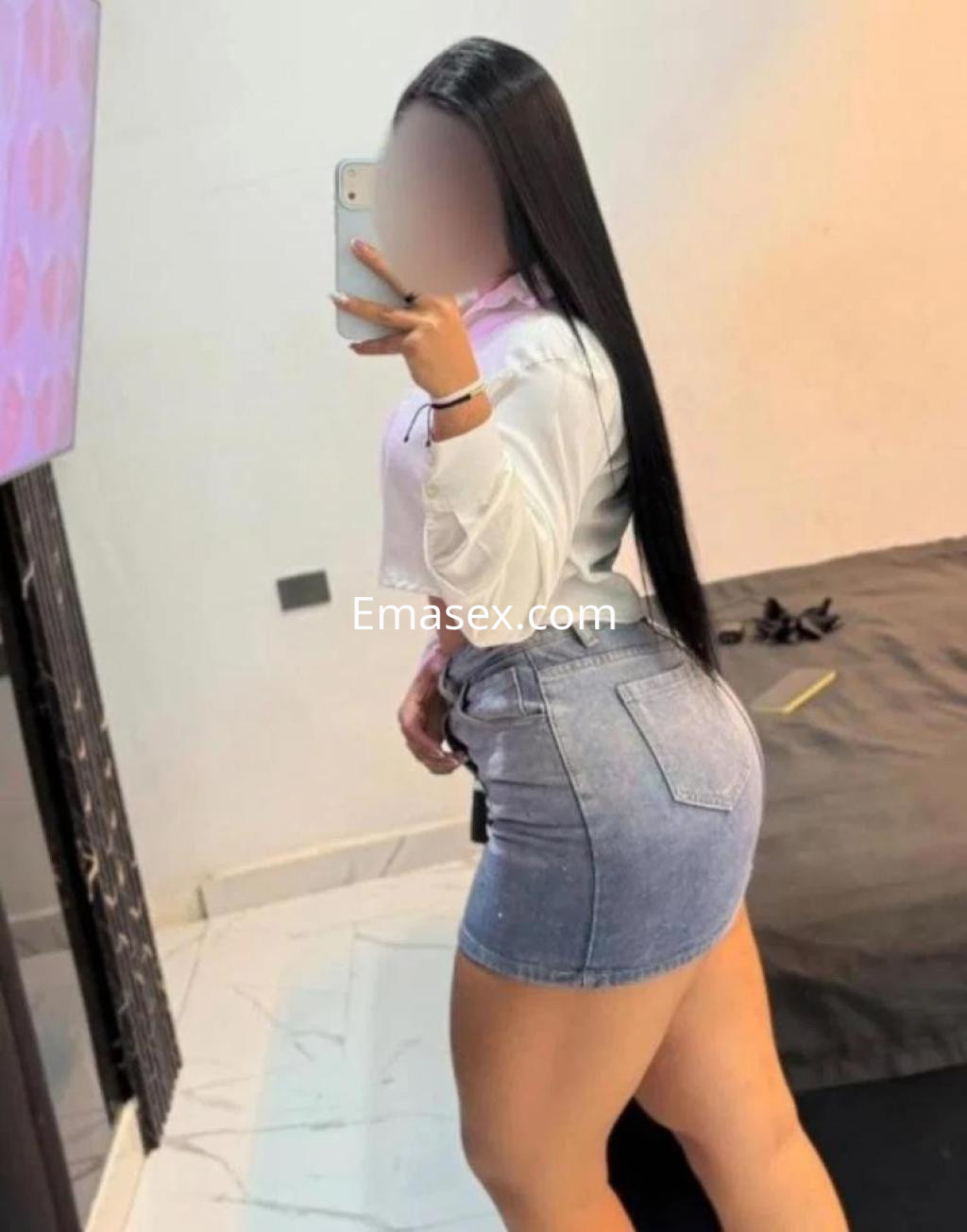 Escort en Lugo posando de espaldas con una blusa blanca y una falda de mezclilla ajustada.