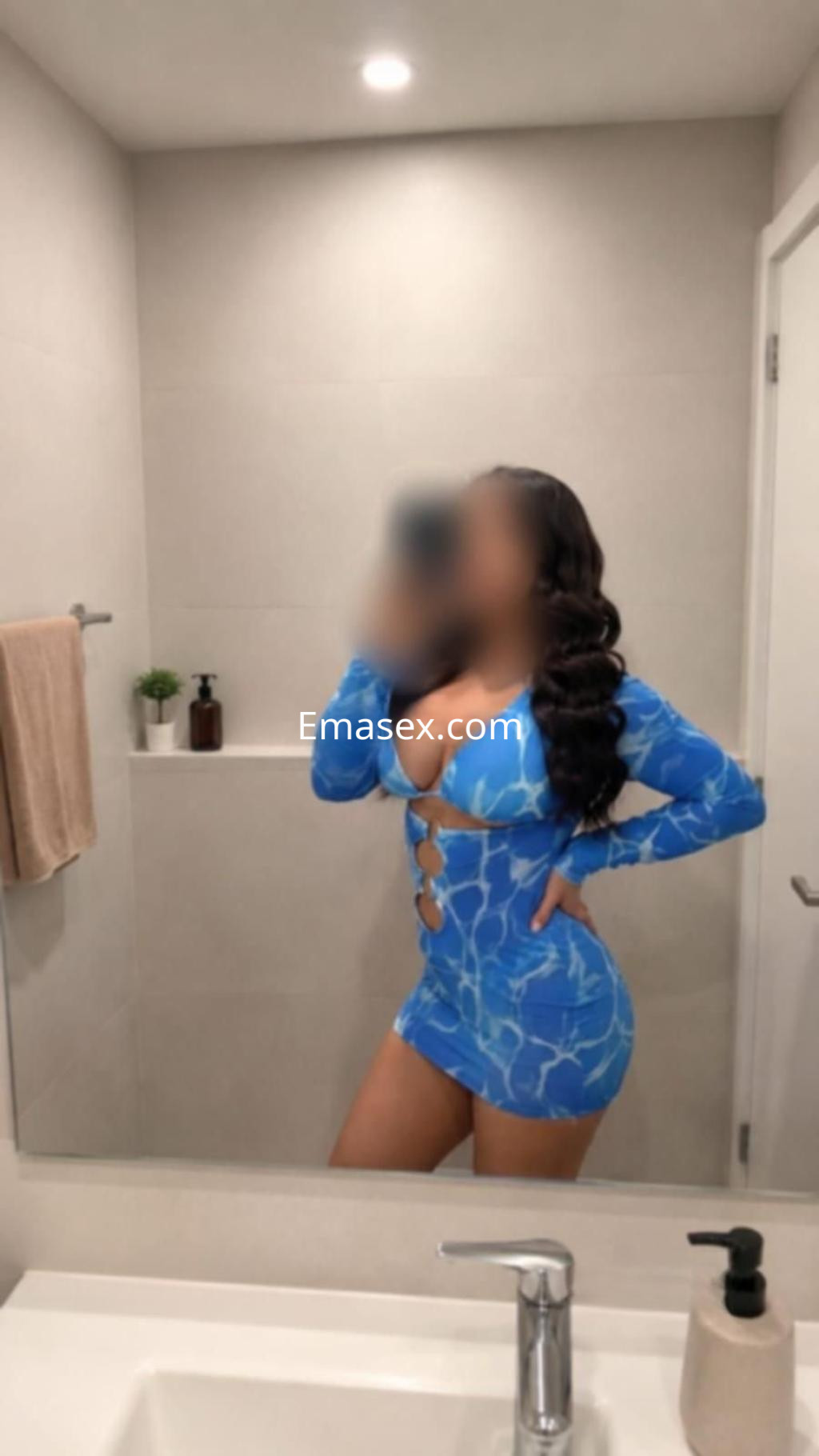 Escort en Madrid luciendo un vestido azul ajustado con cortes, en un baño moderno y bien iluminado.