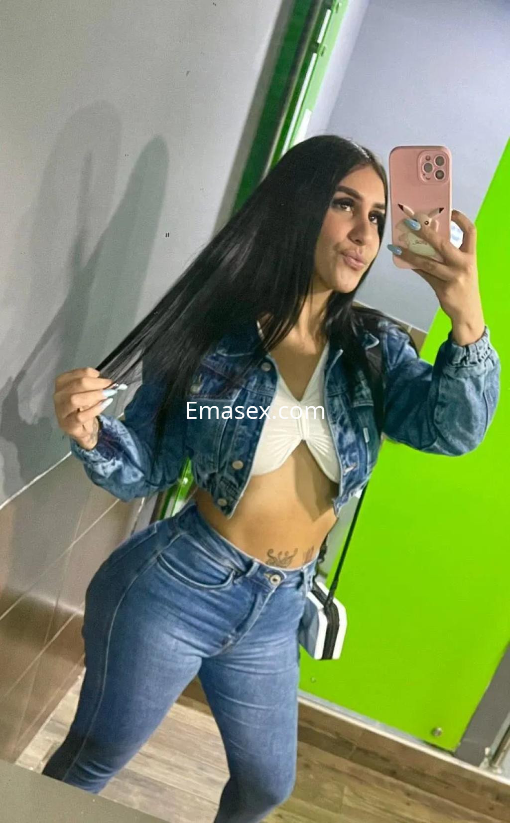 Escort en Málaga con cabello largo y oscuro, vistiendo un top corto y jeans ajustados, posando frente al espejo.