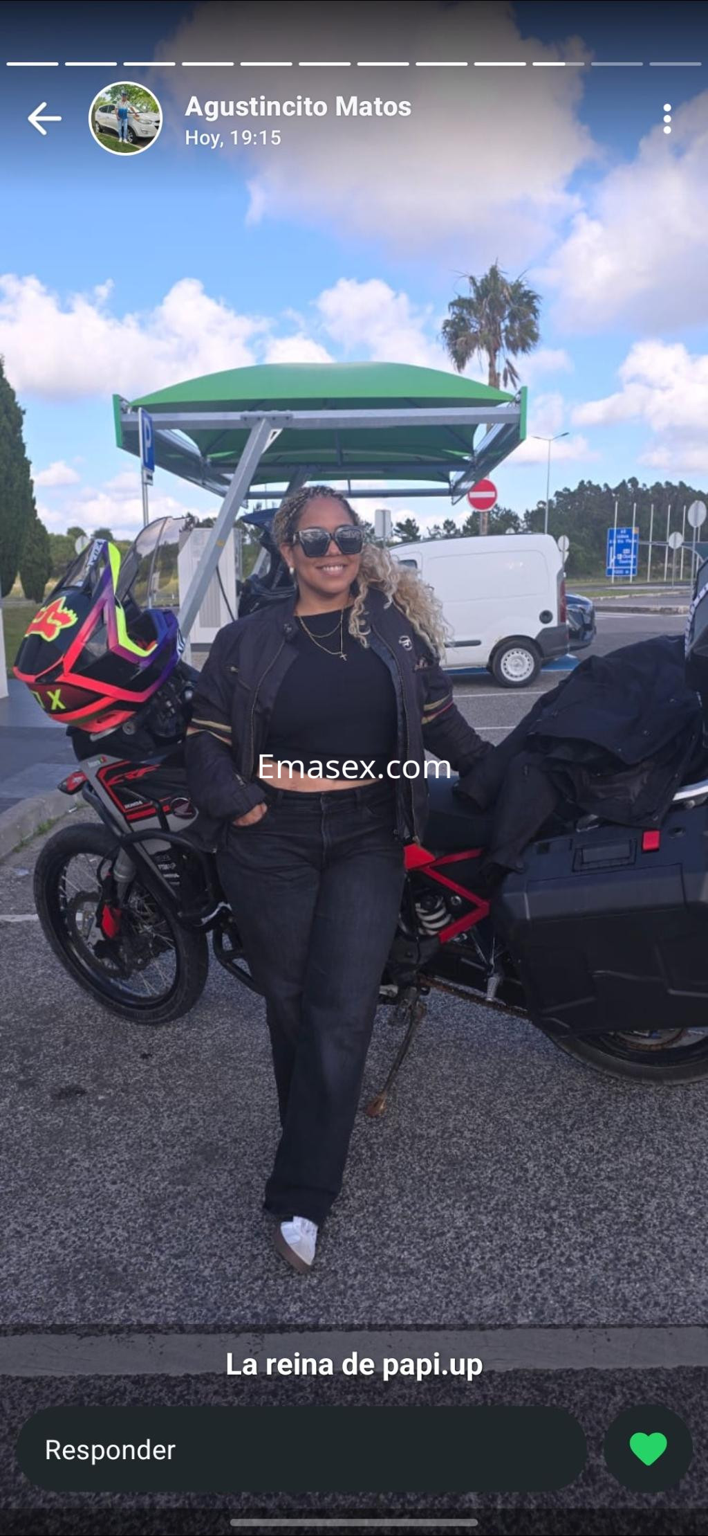 Escort en Gijón posando junto a su moto, vestida con chaqueta negra y jeans, con gafas de sol.