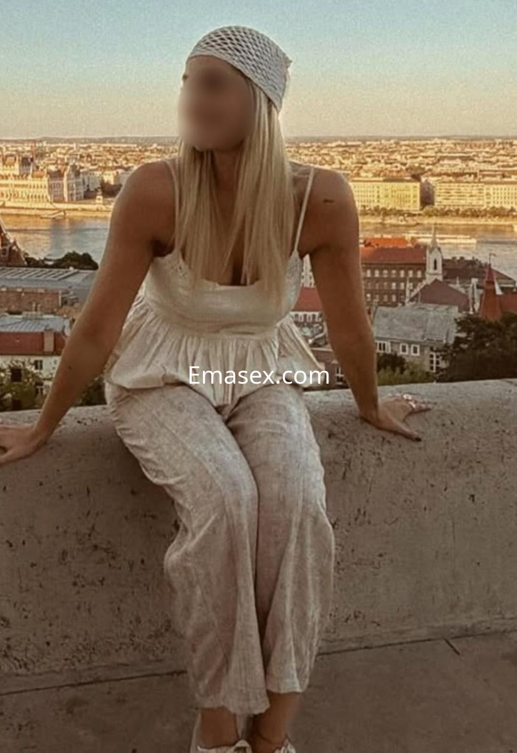 La puta luce una blusa clara y pantalones de lino, sentada en un muro con vista a la ciudad de Salamanca.
