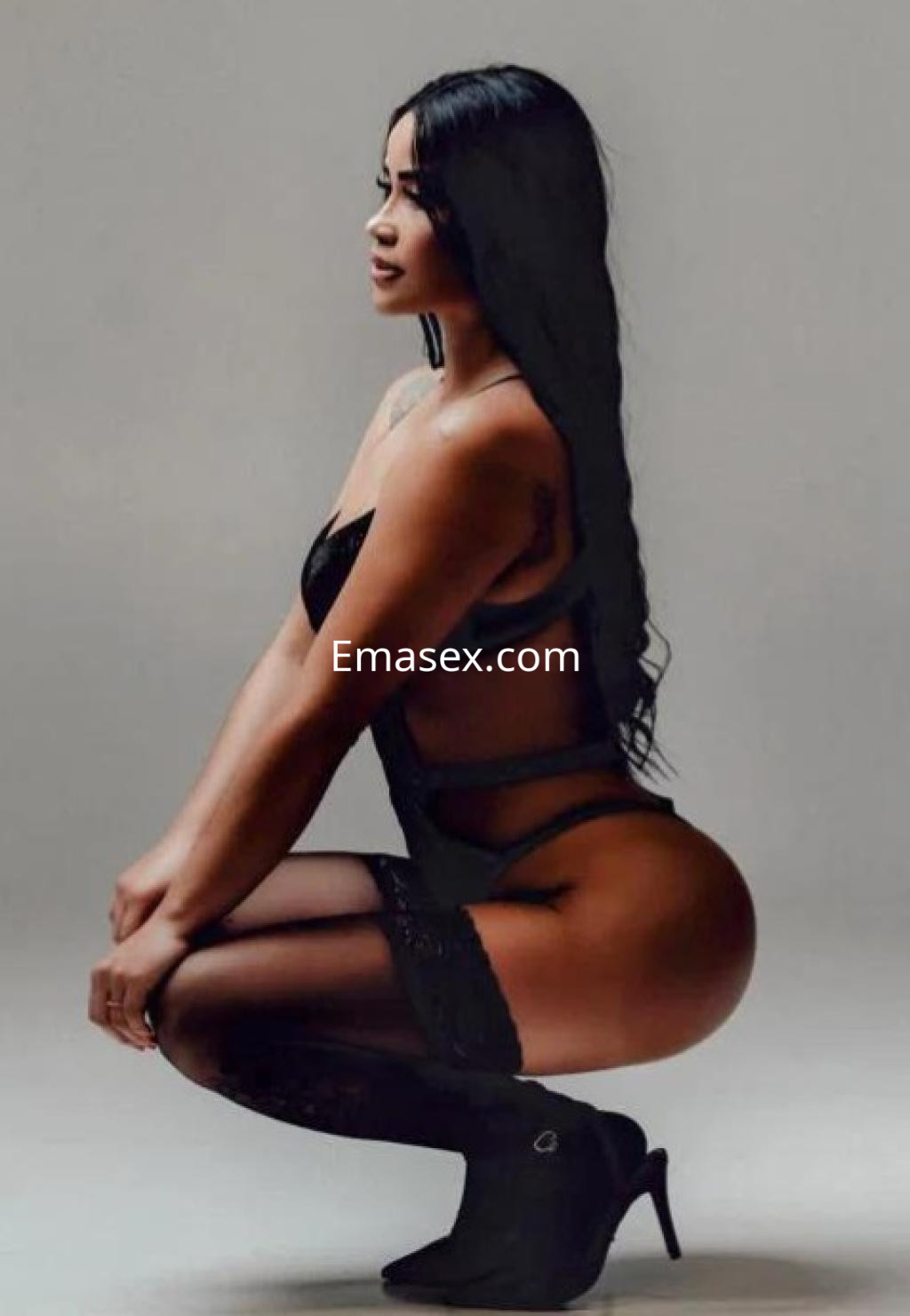 La puta posa de perfil en lencería negra, con medias y tacones, mostrando su figura en Girona.