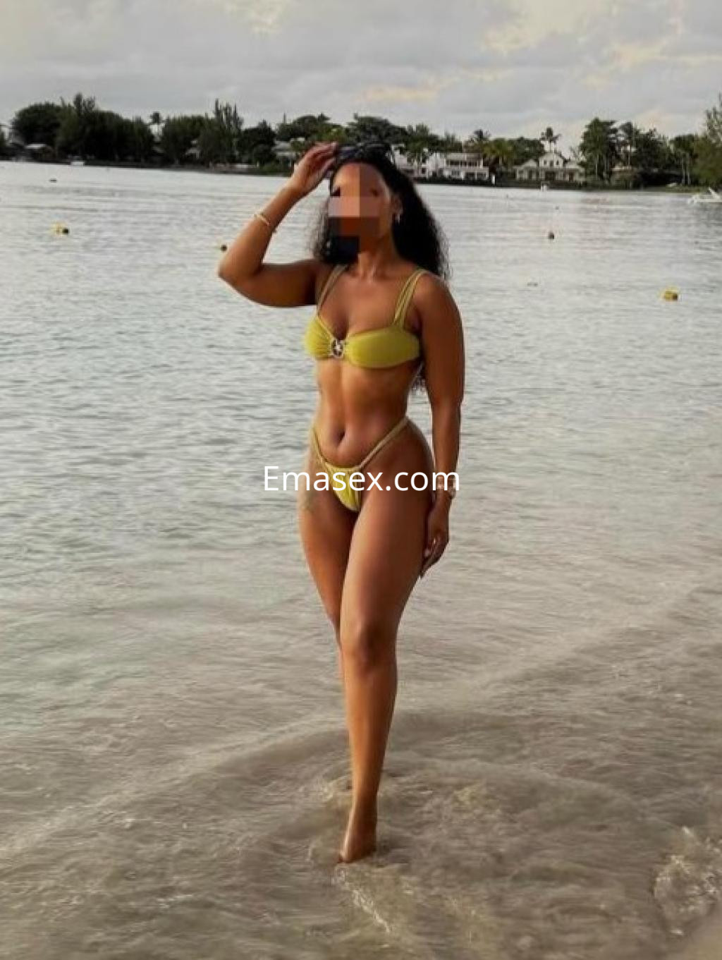 Escort en Girona, de pie en la orilla del mar, luciendo un bikini amarillo y mostrando una figura tonificada.