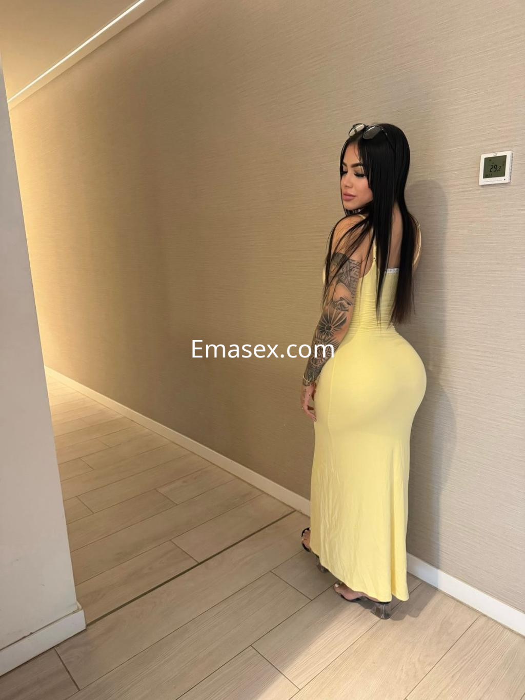 La escort viste un vestido amarilla ajustado y posa de espaldas en un pasillo con paredes claras en Pamplona.
