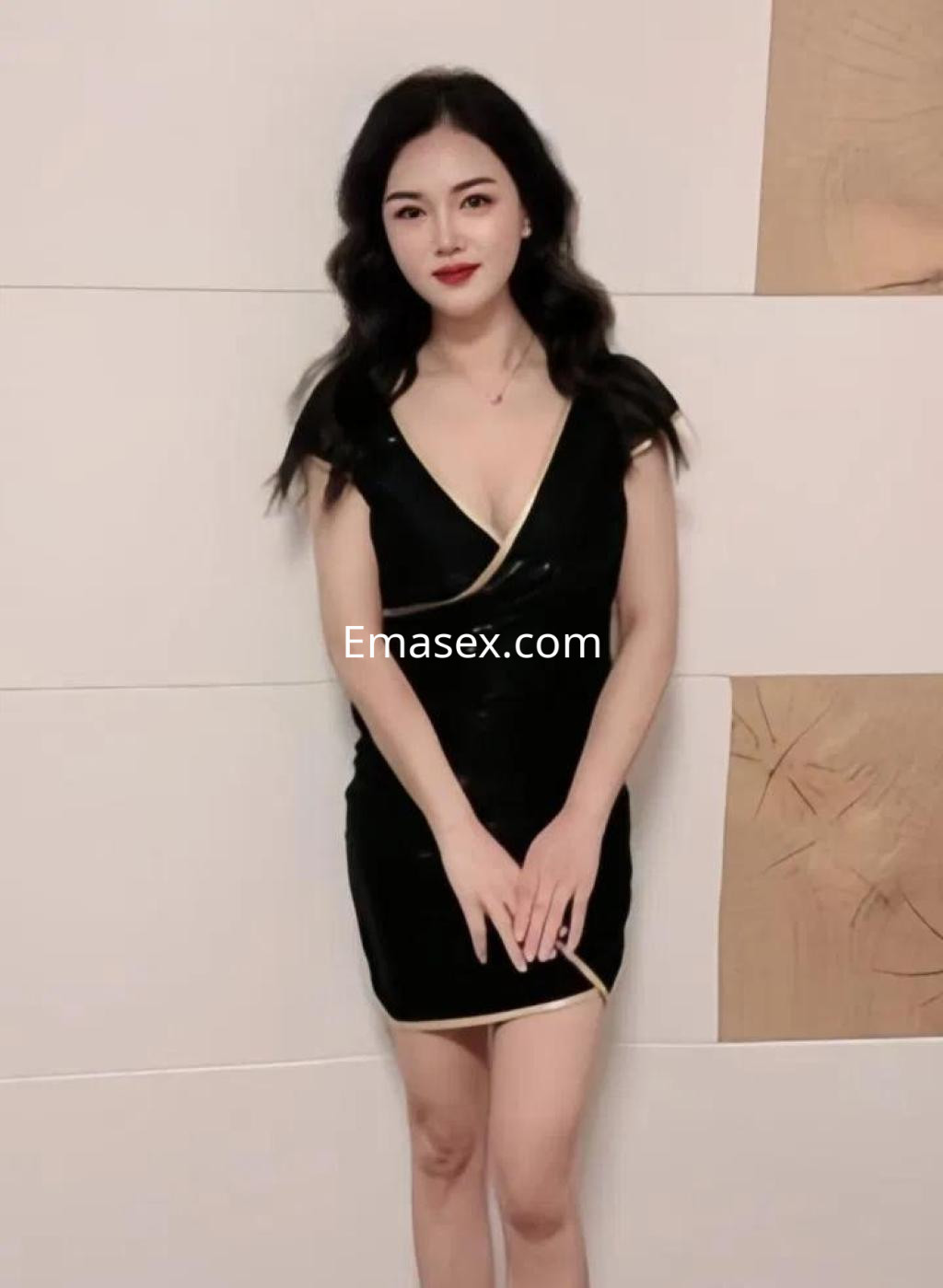 Escort en Barcelona con un vestido negro ajustado y detalles dorados, con cabello ondulado y una pose elegante.