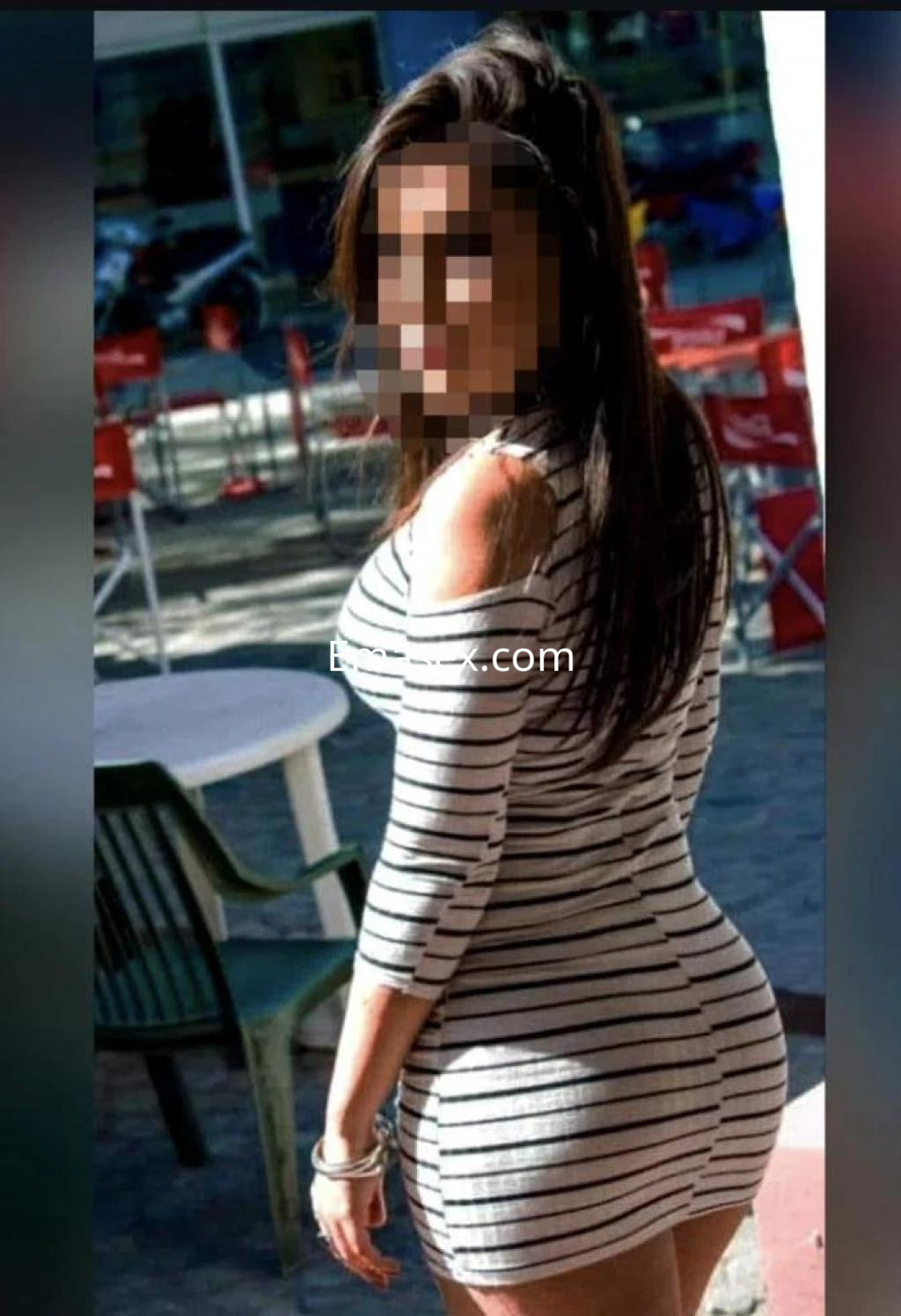 Escort con cabello largo y oscuro, vistiendo un vestido de rayas ajustado, posando de espaldas en Cáceres.