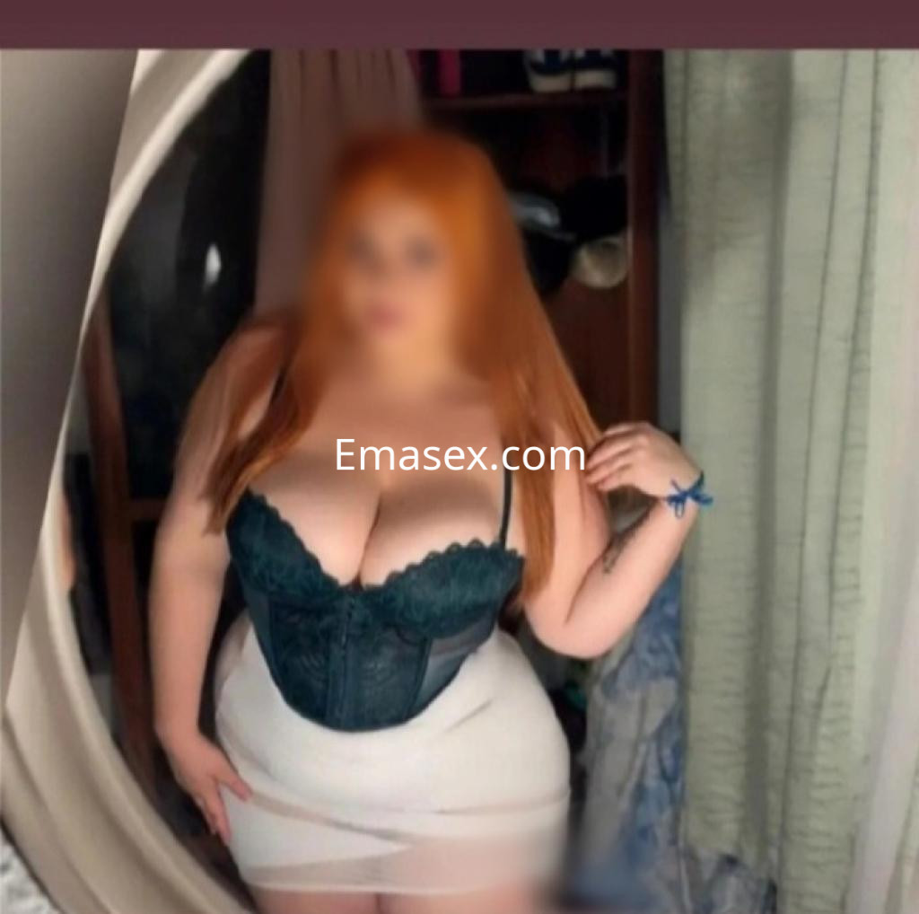 Puta de Lugo posa con un corsé negro con encaje y una falda ajustada, mostrando su cabello largo y pelirrojo.