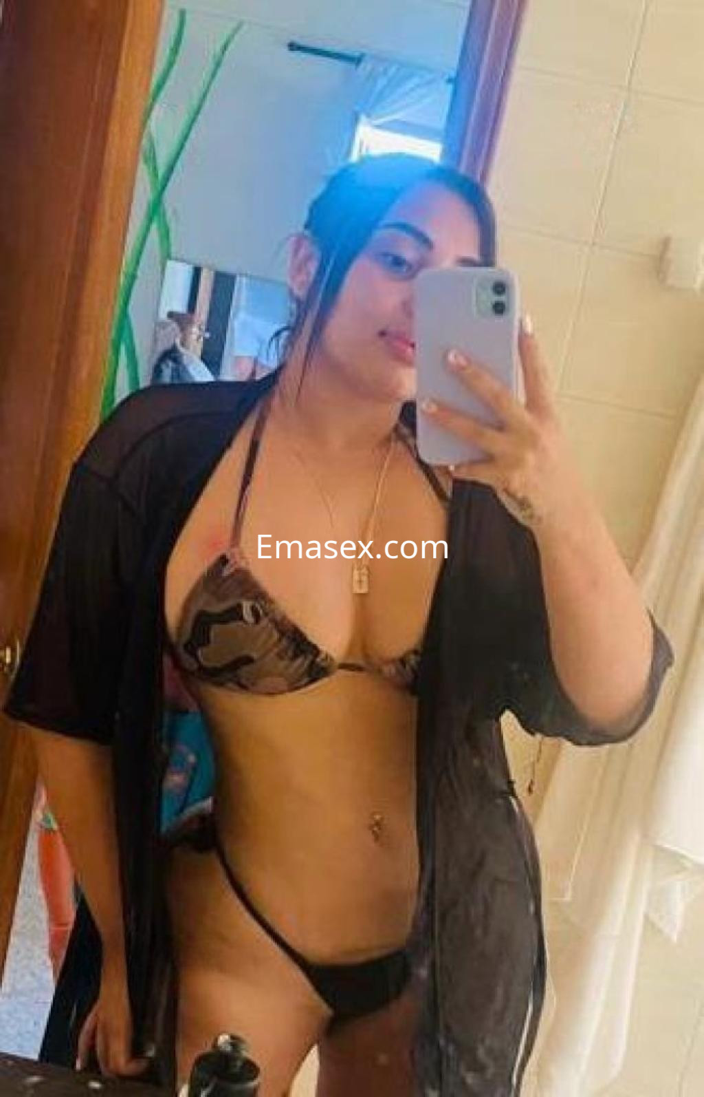 Escort en Madrid posando en un espejo con bikini de camuflaje y una bata negra, mostrando una sonrisa.