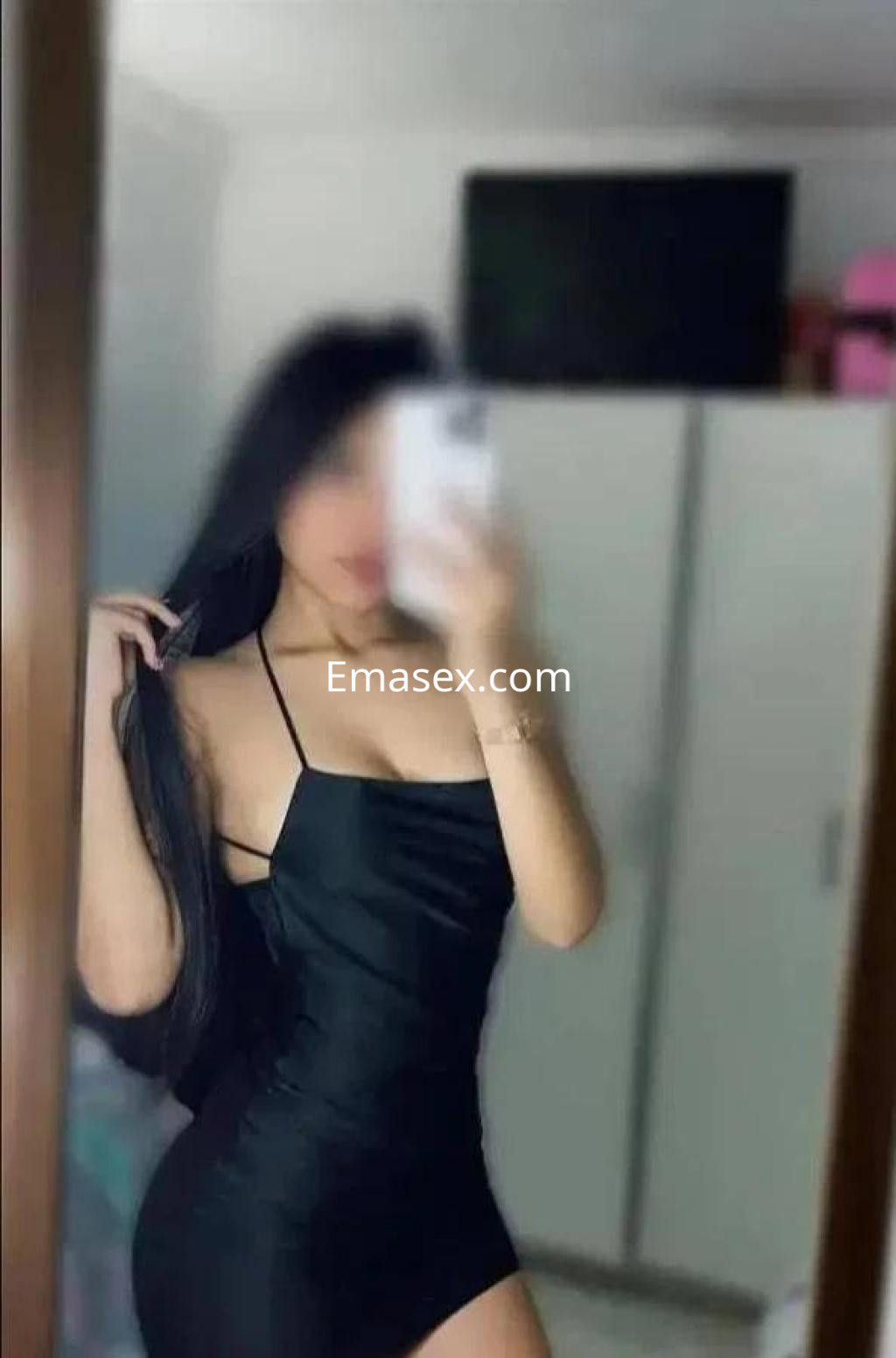 Puta en Sevilla luce un vestido negro ajustado, con tirantes finos, y cabello largo y lacio en un ambiente interior.
