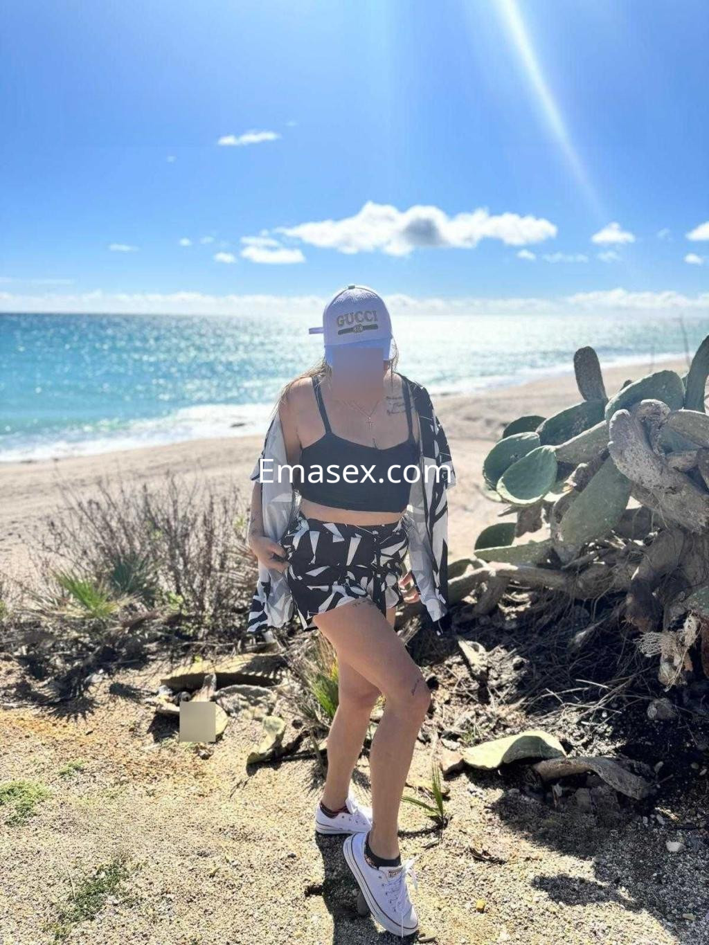Puta en Valencia, luciendo un bañador negro y una camisa ligera, caminando junto a la playa y cactus.