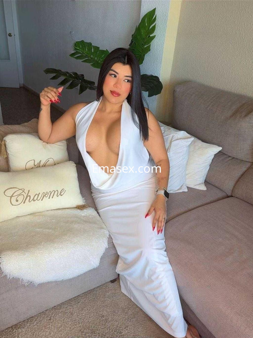 Escort en Almería sentada en un sofá, vistiendo un vestido blanco ajustado y mostrando un escote pronunciado.