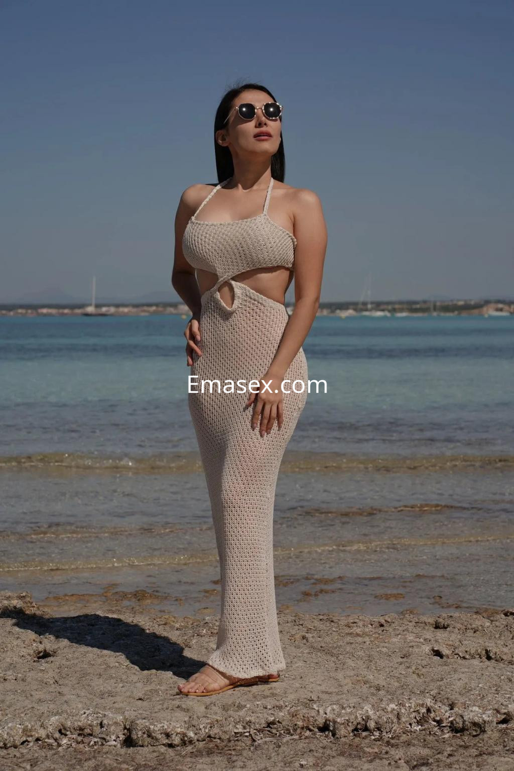 Puta en Palma de Mallorca, luciendo un vestido de red claro y gafas de sol, posando en la playa.