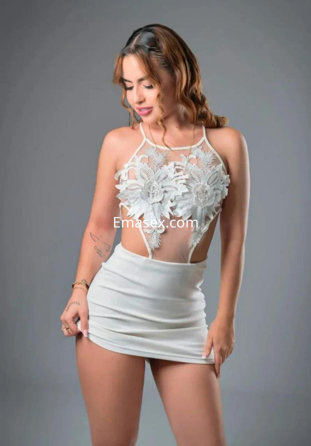 Puta posando en Palma de Mallorca con un conjunto blanco que resalta su figura, sonriendo sutilmente.