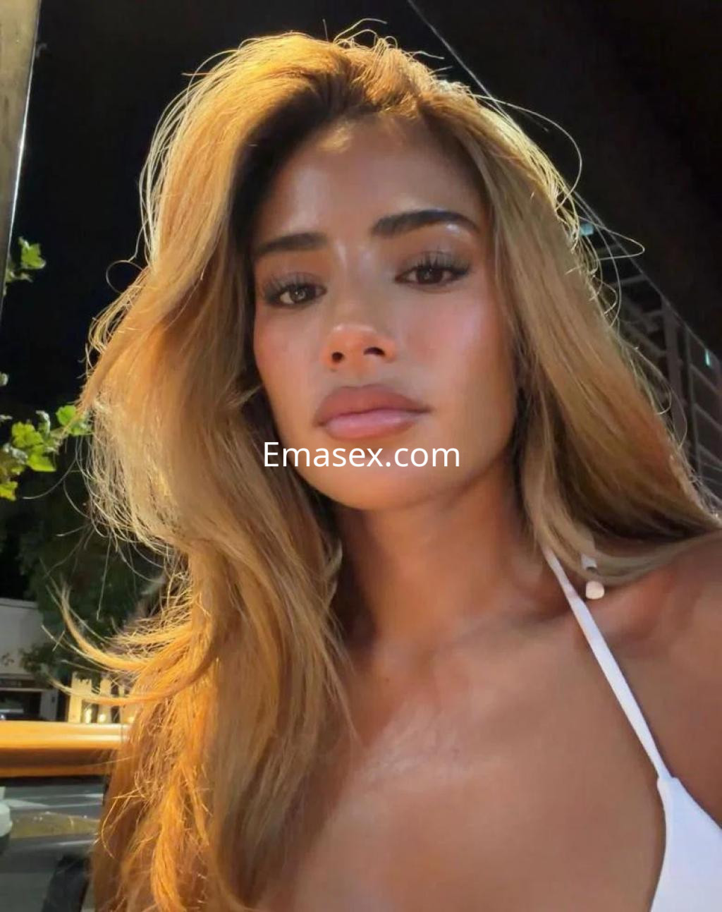 Escort en Barcelona con cabello largo y lacio, luciendo un top blanco, en un ambiente nocturno.