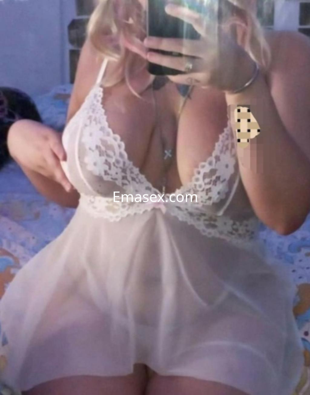 Escort en Coruña con cabello rubio, usando un vestido transparente con detalles de encaje, posando frente a un espejo.
