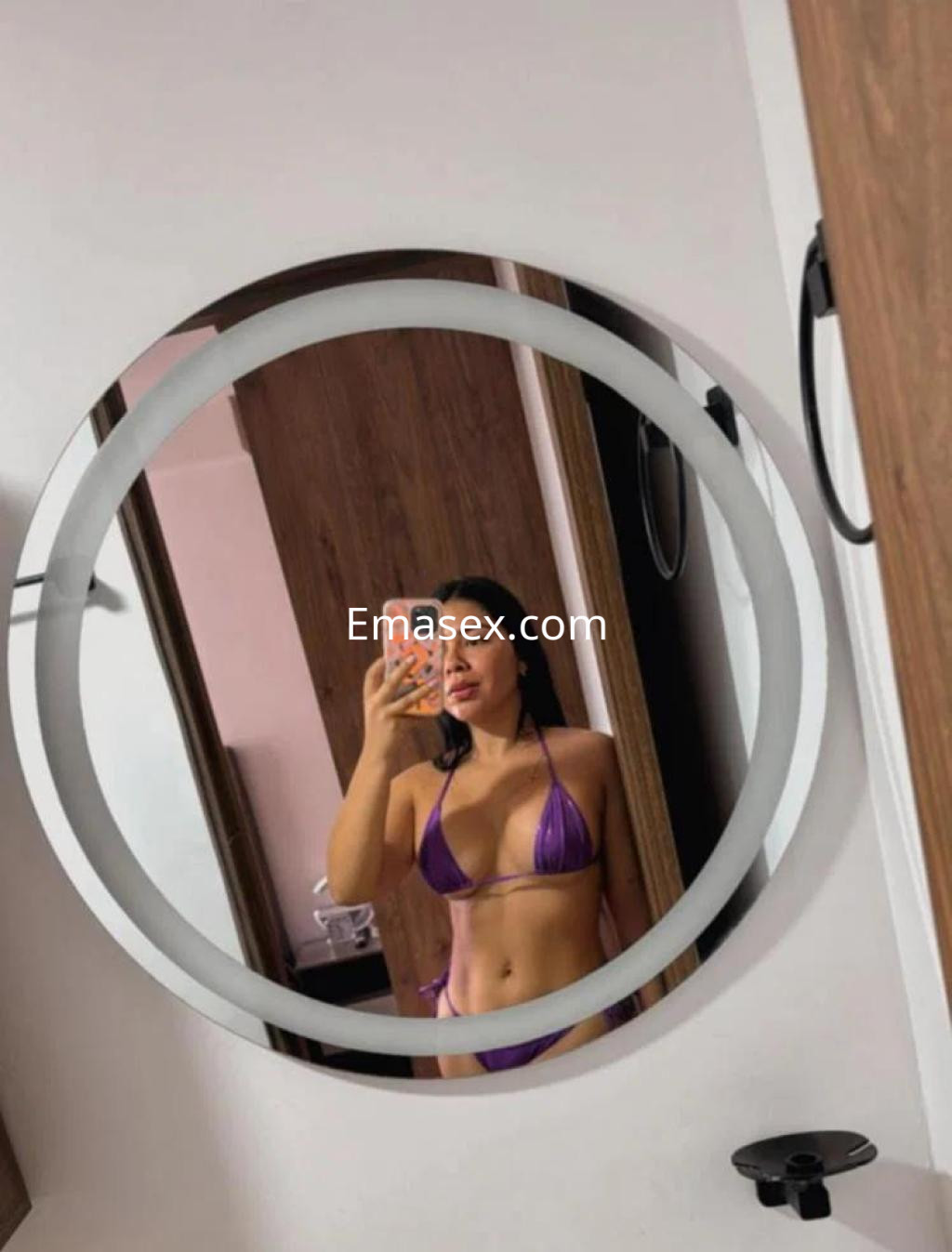 Puta en Coruña se refleja en un espejo, luciendo un bikini morado y mostrando su figura en un entorno moderno.