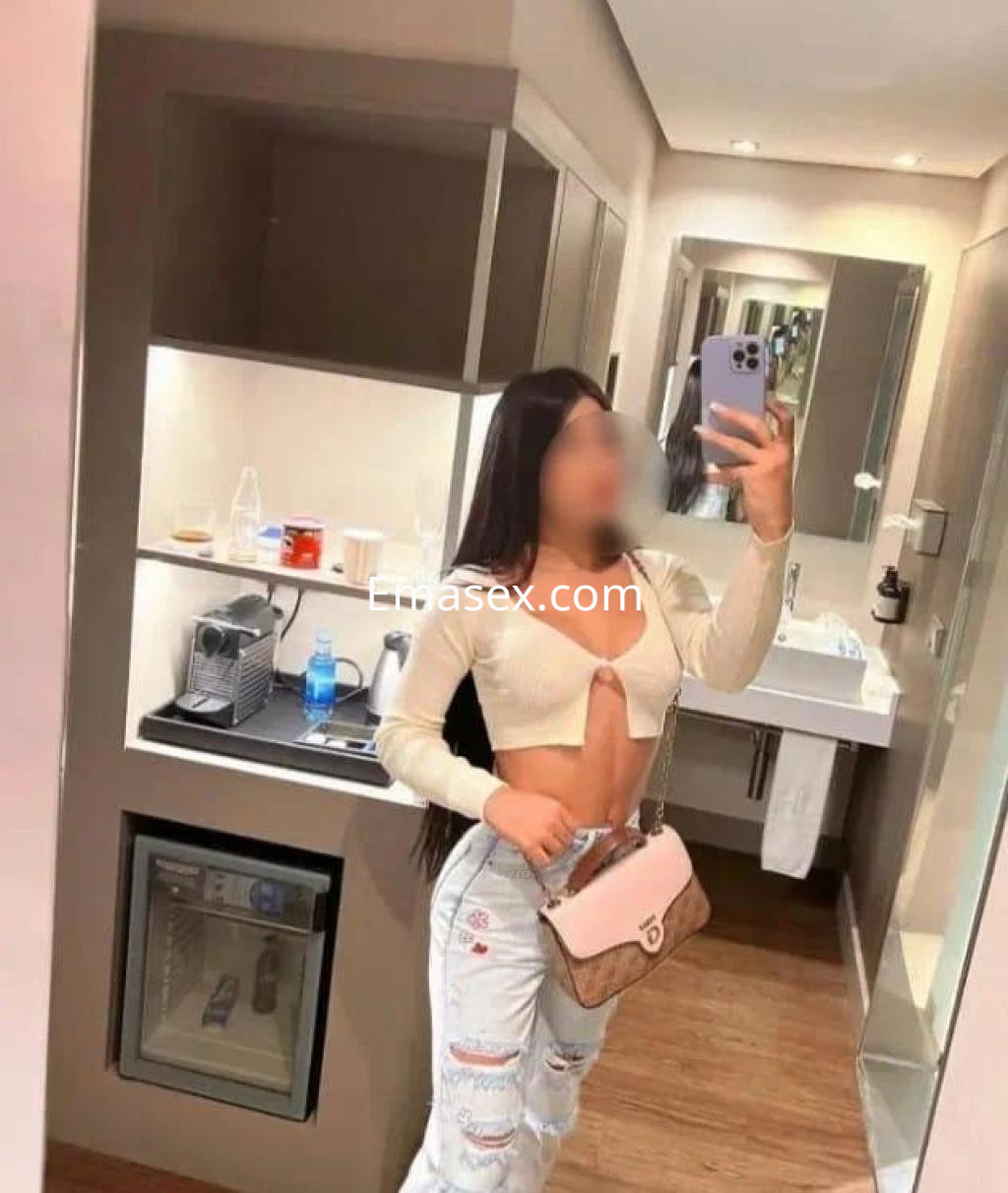 Escort en León con cabello largo y lacio, vistiendo un top claro y jeans, posando en un baño moderno.