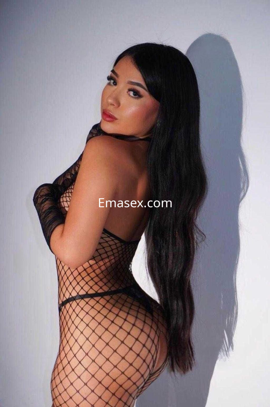 La puta de Murcia posa de perfil, luciendo un body de red negra que resalta su figura y cabello largo.