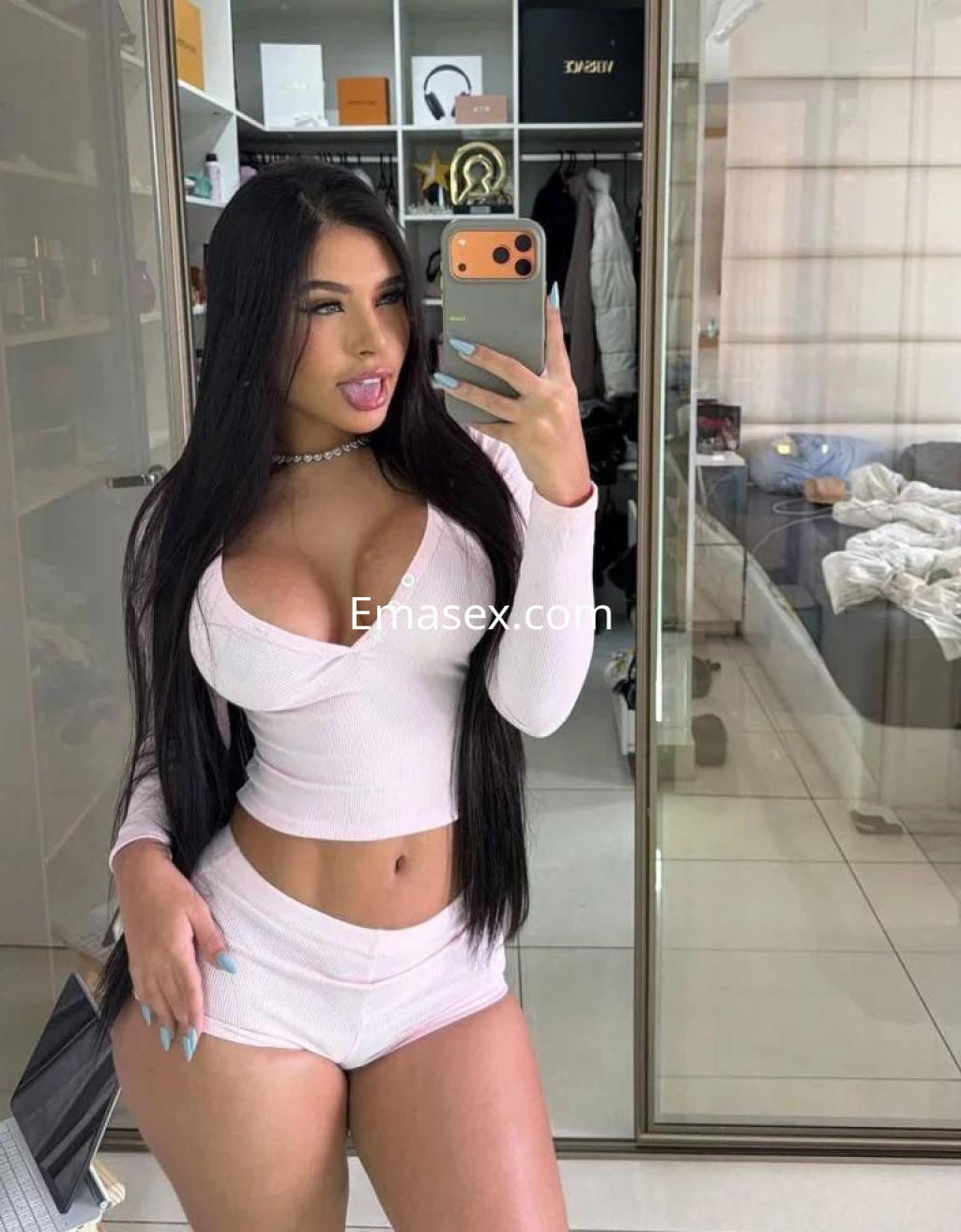 Escort en Murcia con cabello largo y lacio, vistiendo un conjunto rosa claro, posando frente a un espejo.